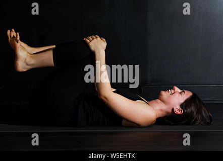 Une belle jeune brunette femme blanche n'postures de yoga sur un fond sombre. Banque D'Images