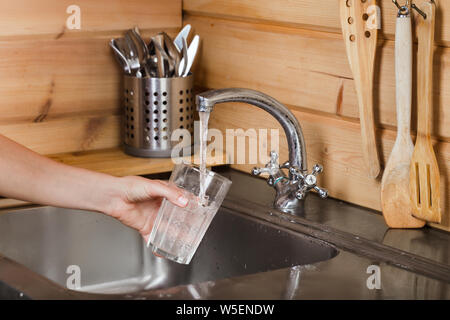L'eau du robinet robinet verse de l'eau dans un verre en main femelle Banque D'Images