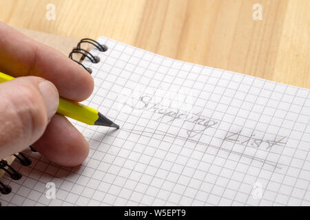 Un homme écrit au crayon jaune sur un ordinateur portable. Inscription Liste d'achat. Close-up Banque D'Images