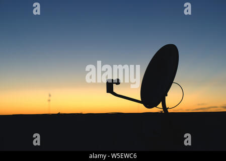 Télévision par satellite dish silhouetté contre le ciel tôt le matin juste quelques minutes avant le lever du soleil. Banque D'Images