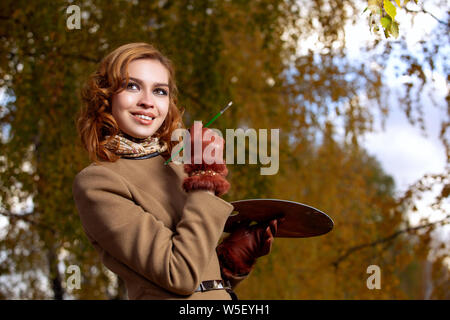 Jeune femme posant avec palette et pinceau en plein air dans le parc de l'automne. Banque D'Images