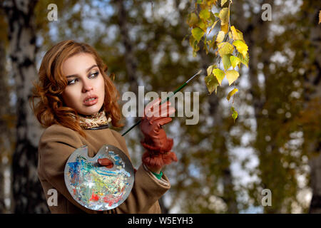 Belle femme avec pinceau et palette de couleurs peintures feuilles des arbres Banque D'Images