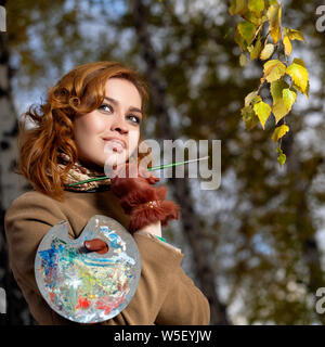 Belle femme avec pinceau et palette de couleurs peintures feuilles des arbres Banque D'Images