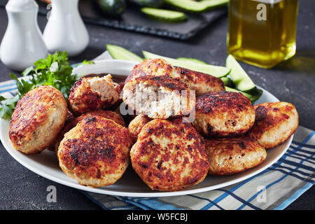 Close-up de galettes de viande polonaise servi avec des tranches de concombre et la sauce barbecue sur une plaque blanche sur une table horizontale de béton, vue de dessus Banque D'Images