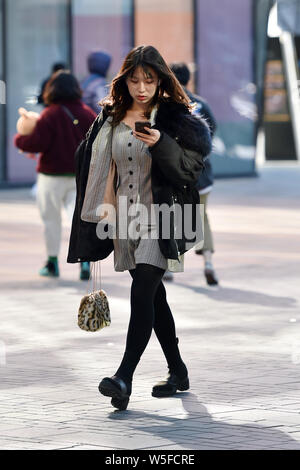 Un jeune Chinois femme marche dans la rue Sanlitun, Beijing, Chine, 21 mars 2019. Un front froid souffle sur la plupart des régions de Ch Banque D'Images