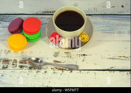 Une tasse de café noir avec boules décoratives sur une soucoupe et un groupe de quatre macarons multicolores. Banque D'Images