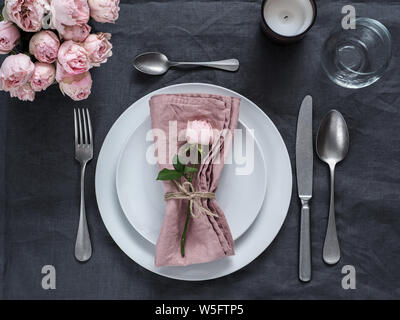 Magnifique table avec bougie sur linge de table gris. Table festive pour le dîner de mariage avec rose vaporisée et serviette rose sur l'assiette. Dîner de vacances avec assiettes blanches Banque D'Images