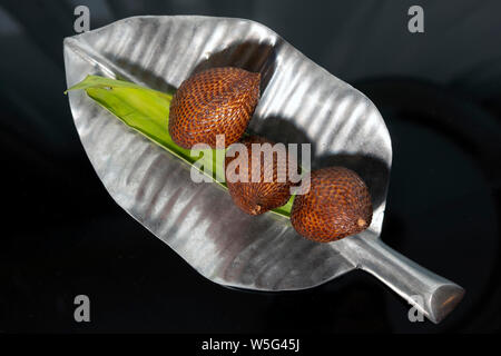 Snakefruit sur une plaque en argent avec la forme de la feuille fond sombre Banque D'Images