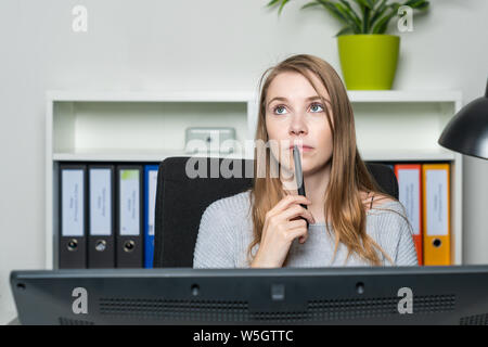 Une jeune femme dans le bureau examine pensivement Banque D'Images