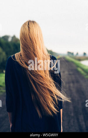 Femme debout aux cheveux longs et à la route de campagne à Banque D'Images