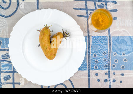 La pomme de terre en forme de coeur organiques sur une plaque blanche sur un tapis tissé naturel. Aimez votre nourriture. Happy Valentine's Day ! Banque D'Images