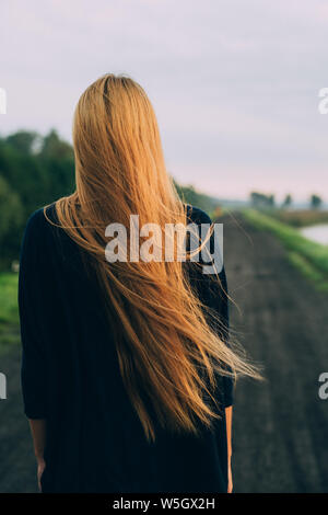 Femme avec de très longs cheveux debout dos à la caméra on country road Banque D'Images