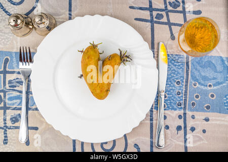 La pomme de terre en forme de coeur organiques sur une plaque blanche sur un tapis tissé naturel. Aimez votre nourriture. Happy Valentine's Day ! Banque D'Images