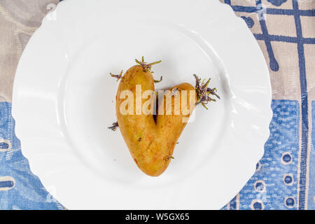 La pomme de terre en forme de coeur organiques sur une plaque blanche sur un tapis tissé naturel. Aimez votre nourriture. Happy Valentine's Day ! Banque D'Images