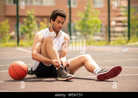 Jeune athlète assis sur un terrain de basket-ball et d'attacher les lacets de chaussures Banque D'Images