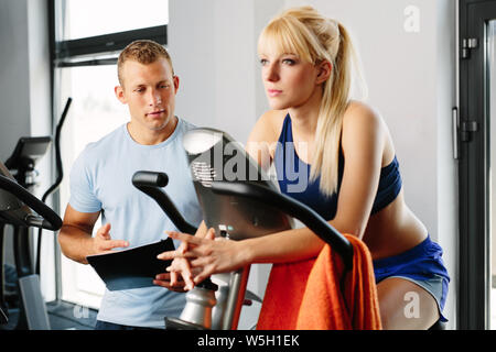 Entraîneur personnel et young blonde woman spinning sur un vélo dans un studio de remise en forme Banque D'Images