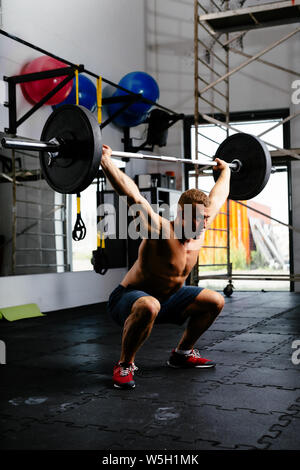 L'homme musclé faisant squats avec barbell in a gym Banque D'Images