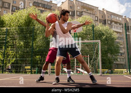 L'un des joueurs de basket-ball avec ballon en essayant de ne pas laisser son rival à emporter Banque D'Images