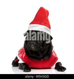 Chiot pug déterminé à la recherche sur le côté et les sourcils tout en portant un chapeau de Noël et de l'enveloppe et couché sur fond studio blanc Banque D'Images