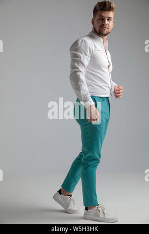 L'homme indifférent à l'autre et regardant par-dessus son épaule tout en portant une chemise blanche et un jean Gris sur fond de studio Banque D'Images