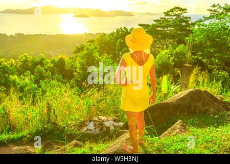 Femme en robe jaune touristiques bénéficiant de vue de l'île de Praslin haut Vue de La Digue au coucher du soleil, les Seychelles, océan Indien, Afrique Banque D'Images