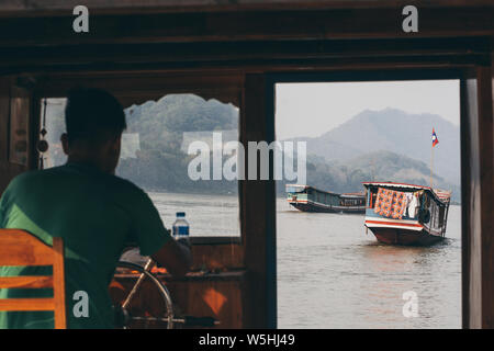 Luang Prabang, Laos - Mai 2019 : vue sur les bateaux traditionnels en bois laotien lent sur le fleuve du Mékong à travers la fenêtre du capitaine de pilotage. Banque D'Images