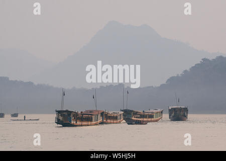 Bateaux traditionnels en bois laotien lent sur le fleuve du Mékong près de Luang Prabang, Laos, au coucher du soleil. Arrière-plan sur la montagne Banque D'Images