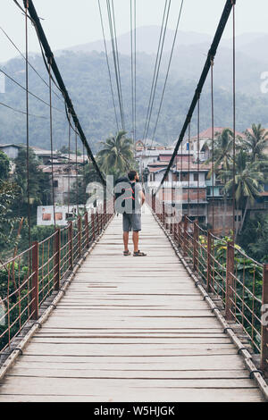 Sac à dos avec l'homme debout sur le pont suspendu en bois dans un village de montagne amoing jungles laotien au Laos. Orientation verticale Banque D'Images