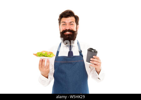 Cafe food concept. Homme garçon barbu tablier porter porter la plaque avec la nourriture et tasse à café. Profitez de votre repas. Guy servant un croissant fourré la laitue et les légumes frais. Alimentation saine. De délicieux croissants. Banque D'Images