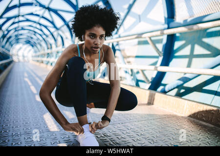 L'accent femme africaine à porter son lacet de liage de remise en forme. Femme Fitness de serrer ses chaussures avant un sprint. Banque D'Images