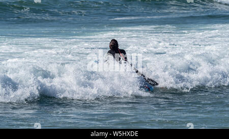 Piscine d'un surfer à travers les vagues sur la plage de Borderia dans l'Algarve, Portugal Banque D'Images