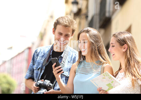 Groupe de trois heureux touristes localiser à l'aide de smart phone et carte papier dans la rue en vacances Banque D'Images