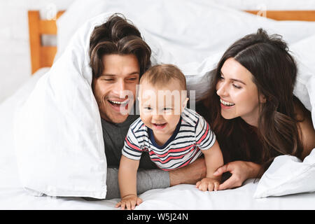 Cheerful parents jouant avec son bébé au lit Banque D'Images