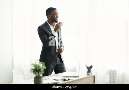 Handsome african american businessman drinking coffee près de window in office Banque D'Images