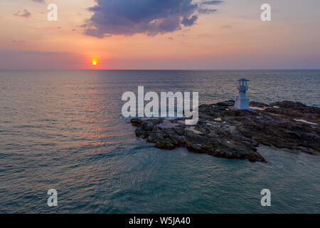 Drone aérien vue d'un coucher du soleil tropical derrière un petit phare sur une île rocheuse Banque D'Images
