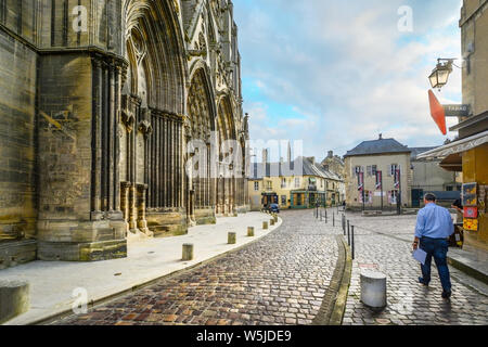 Un homme marche à travers la petite place faisant face à la façade de Notre Dame de la cathédrale de Bayeux en Normandie France Banque D'Images