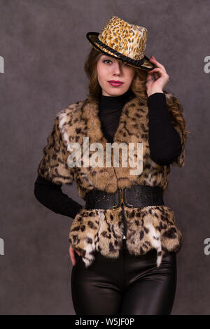 Modèle fille en manteau de fourrure et Leopard Hat posing sur fond gris dans le studio Banque D'Images