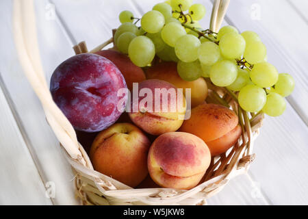 Les abricots mûrs, prune et raisin vert blanc dans un petit panier, selective focus sur le fond en bois blanc Banque D'Images