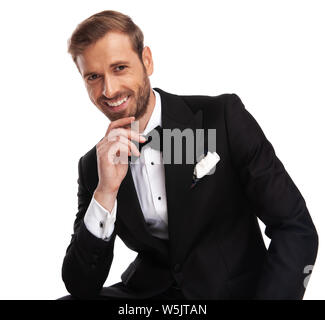 Portrait of pensive businessman en costume noir assis sur fond blanc et souriant Banque D'Images