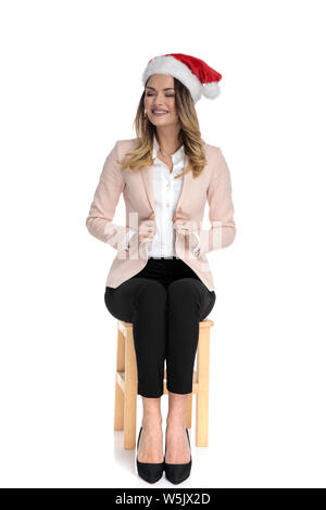 Joyeux businesswoman with santa hat costume rose détient le collier avec les yeux fermés, assis sur chaise en bois Banque D'Images