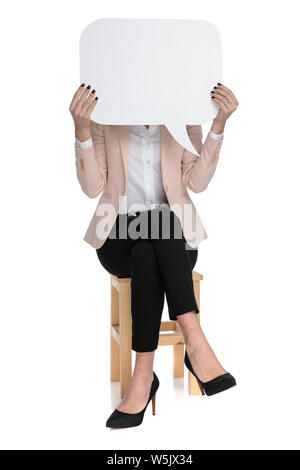 Smart casual femme bulle devant son visage alors qu'il était assis avec les pieds repliés sur fond blanc, Banque D'Images