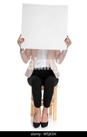 Smart casual woman sitting on stool est titulaire d'annonce sur fond blanc Banque D'Images