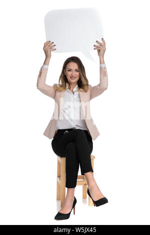 Young businesswoman wearing High heels et costume rose est assise sur chaise de bois et est titulaire d'bulle en l'air sur fond blanc, pleine longueur photo Banque D'Images