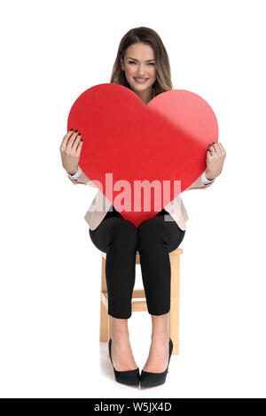 Les jeunes smart casual femme grande saint-valentin coeur tout en restant assis sur tabouret en bois sur fond blanc Banque D'Images