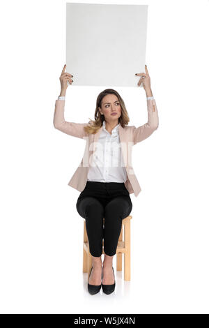 Curieux smart casual femme plateau vide et ressemble à l'autre tout en restant assis sur le tabouret en bois sur fond blanc Banque D'Images