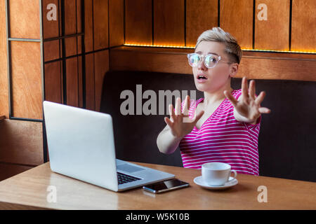 Stop ! Portrait de jeune fille peur émotionnelle indépendant avec cheveux courts, en t-shirt rose est assise dans un café et crier avec les bras levés et le stress Banque D'Images