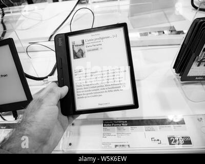 Paris, France - Jul 25, 2019 : man main tenant la lecture de l'eReader Kobo Forma est un e-reader produites par l'entreprise torontoise Kobo Inc en français supermarché électronique FNAC - noir et blanc Banque D'Images