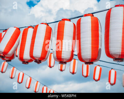 Rouge-blanc papier lanternes Chochin japonais accroché sur fond de ciel bleu nuageux. Fond d'été Banque D'Images