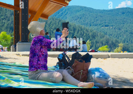 Une femme asiatique assis sur une serviette de plage tout en tenant un. selfies Banque D'Images