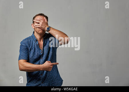 Un homme en habits cache son visage avec ses mains sur un fond gris. Émotif, brave face. Isolé sur fond blanc Copy space Banque D'Images